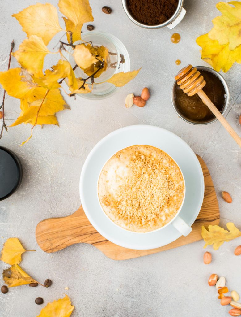 Warm cup of coffee garnished with honey and autumn leaves in a cozy flat lay setting.